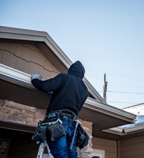 contractor installing gutters on a residential building in the winter with snow on the roof.
